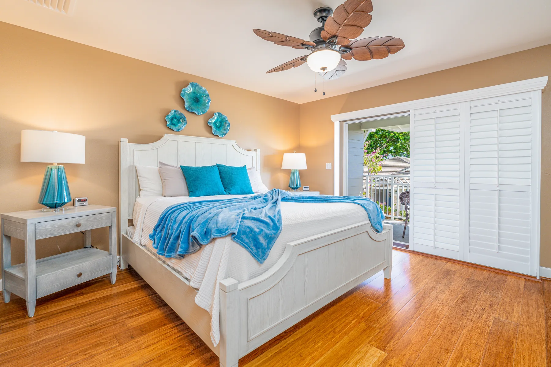 A bright bedroom features a white bed with blue bedding and a ceiling fan.