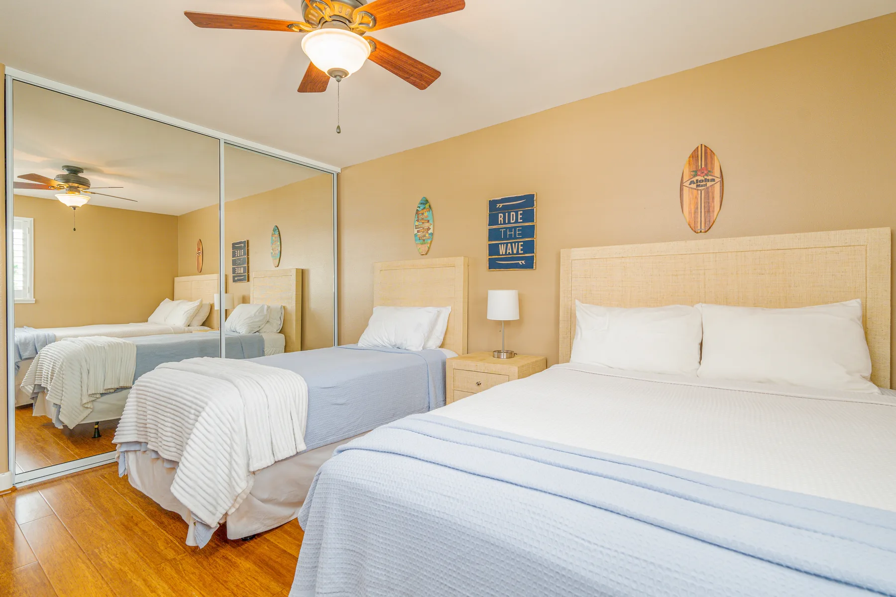 A bedroom with two beds, mirrored closet doors, and a ceiling fan.