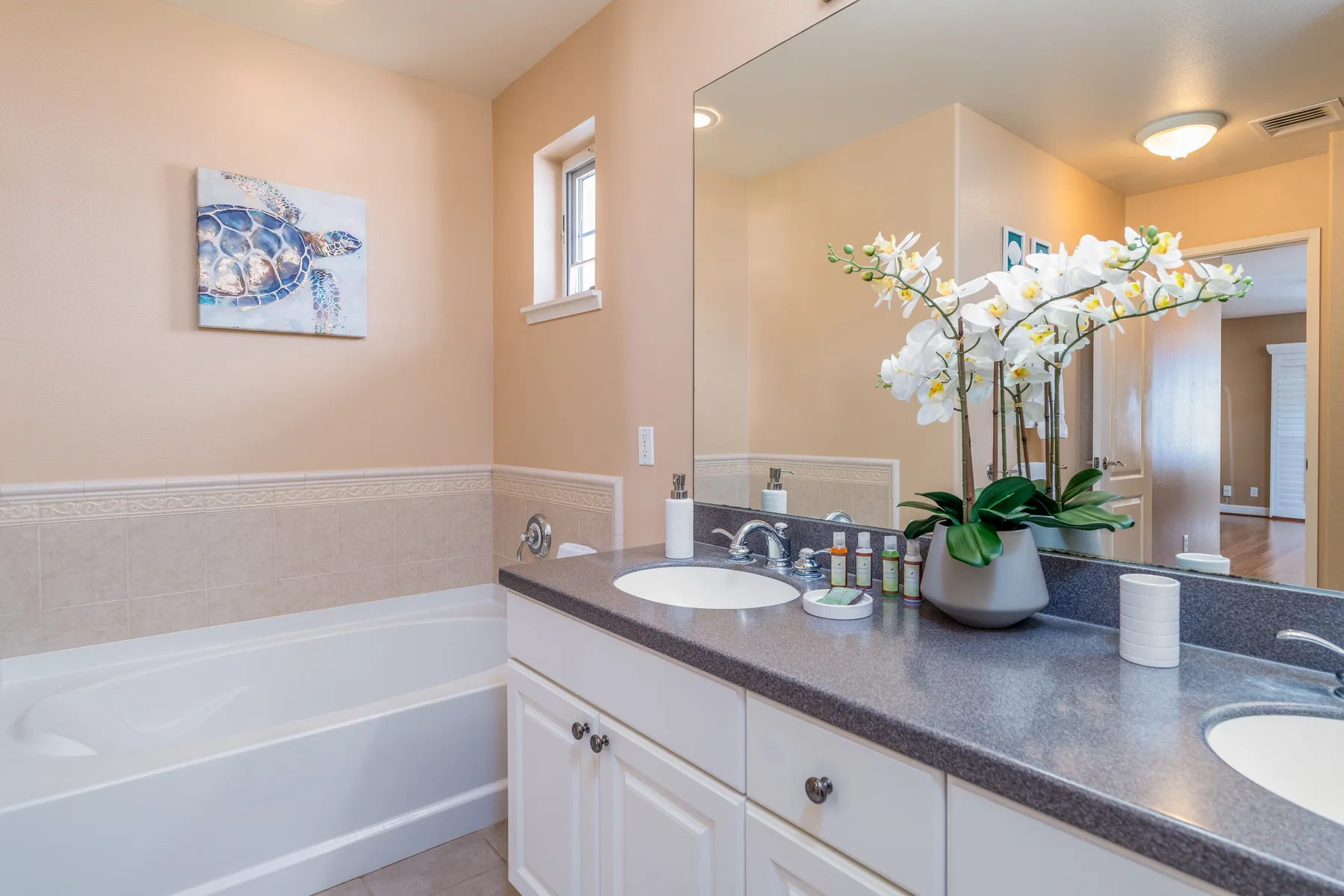 A bathroom vanity with a sink and orchid sits beside a bathtub.
