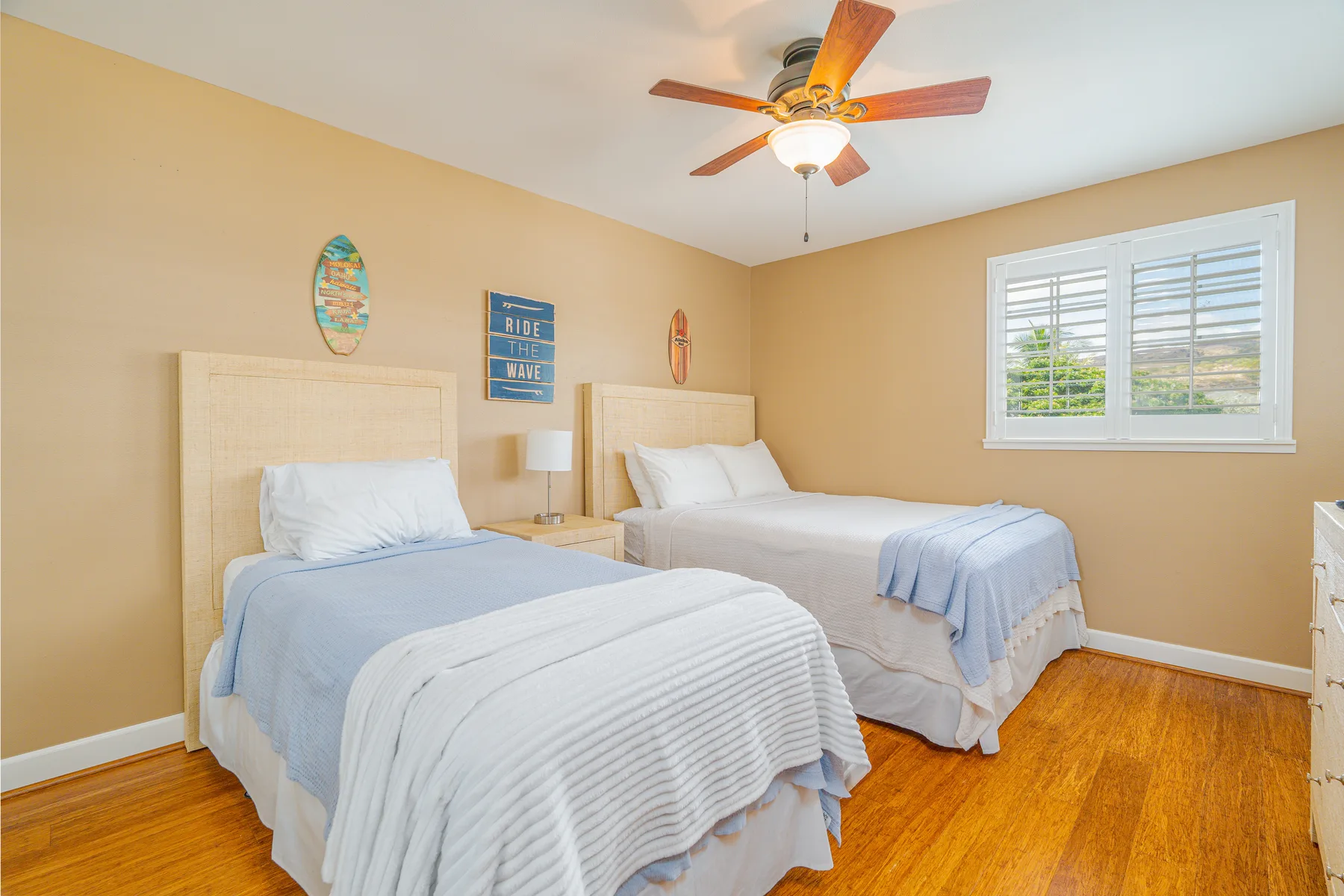 A bedroom with two beds, pale bedding, and a ceiling fan.