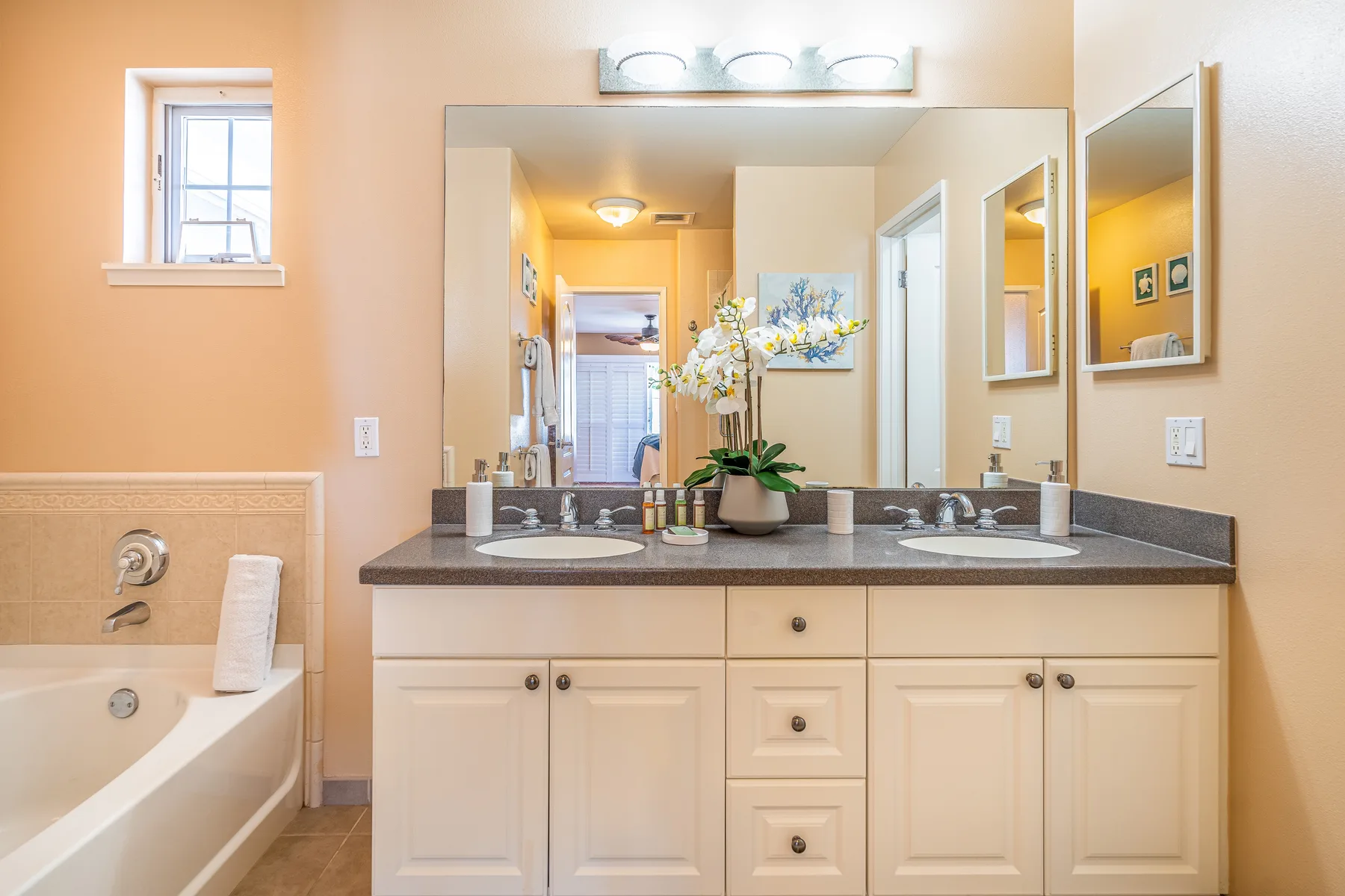 A bathroom vanity with a wide mirror and a bathtub beside it.