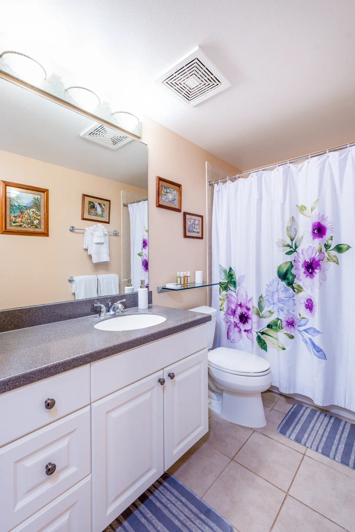 A bathroom vanity and sink sit beside a toilet and a floral shower curtain.