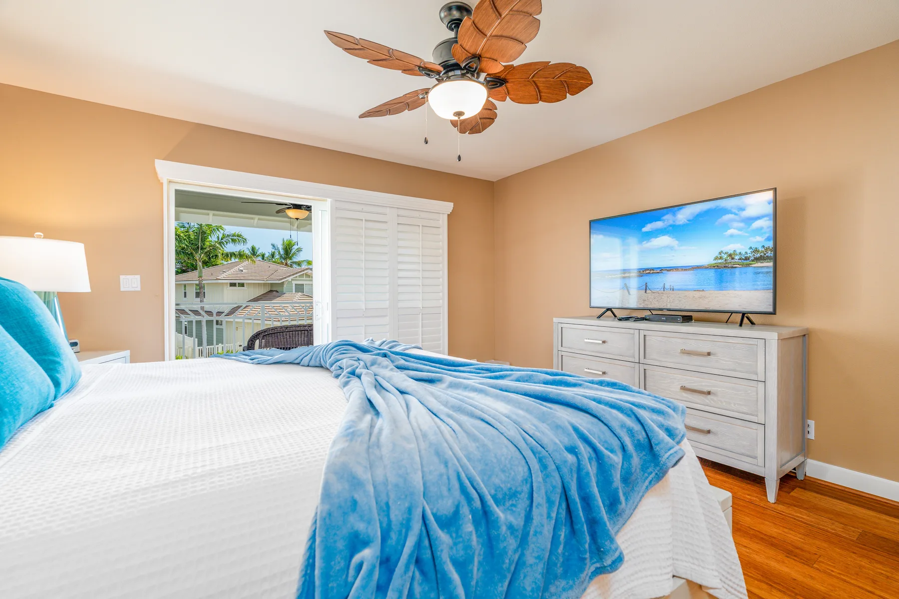 A bedroom with a bed covered by a blue blanket and a television on a dresser.
