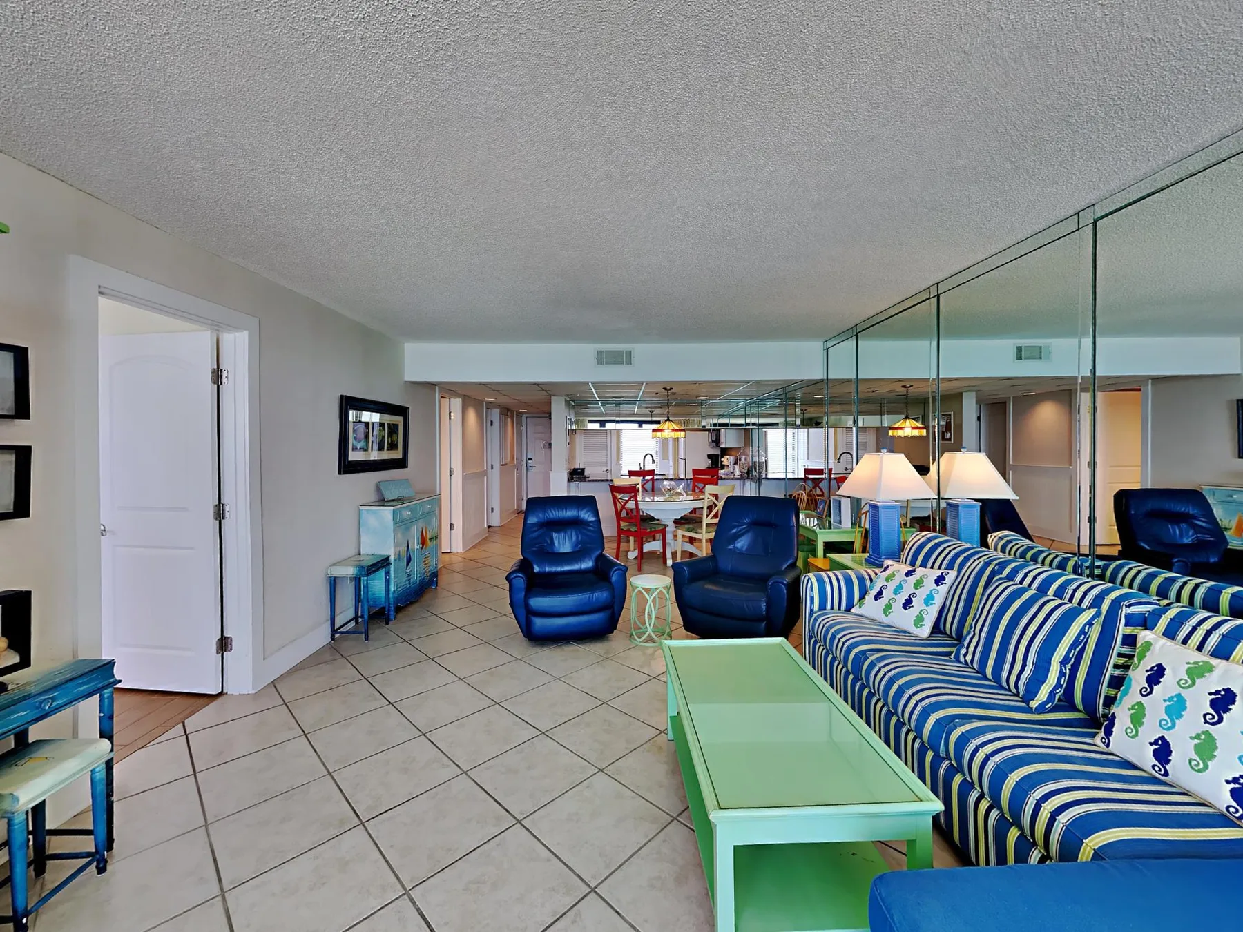 A living room with striped seating, a glass coffee table, and tiled flooring.