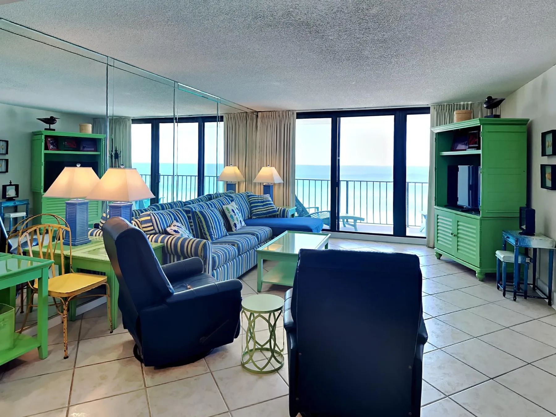 Sala de estar con asientos, un mueble para televisión y grandes ventanas con vista al agua.