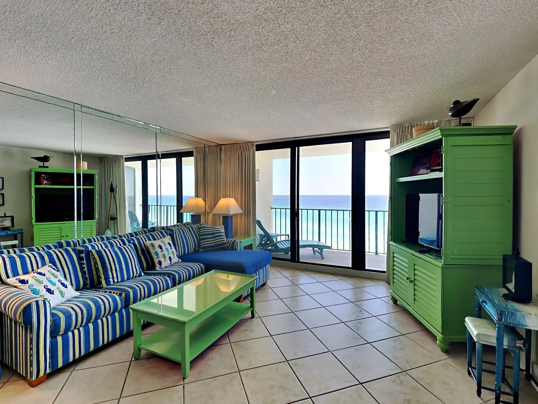 A living room with striped seating, green furniture, and sliding glass doors overlooking the water.