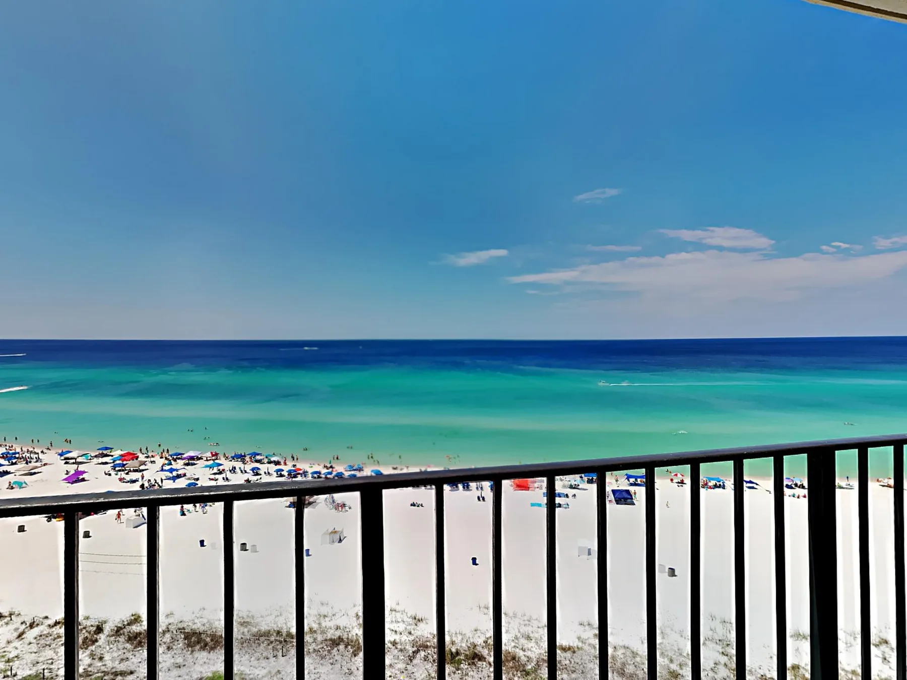 A beach and turquoise water are visible beyond a black balcony railing.