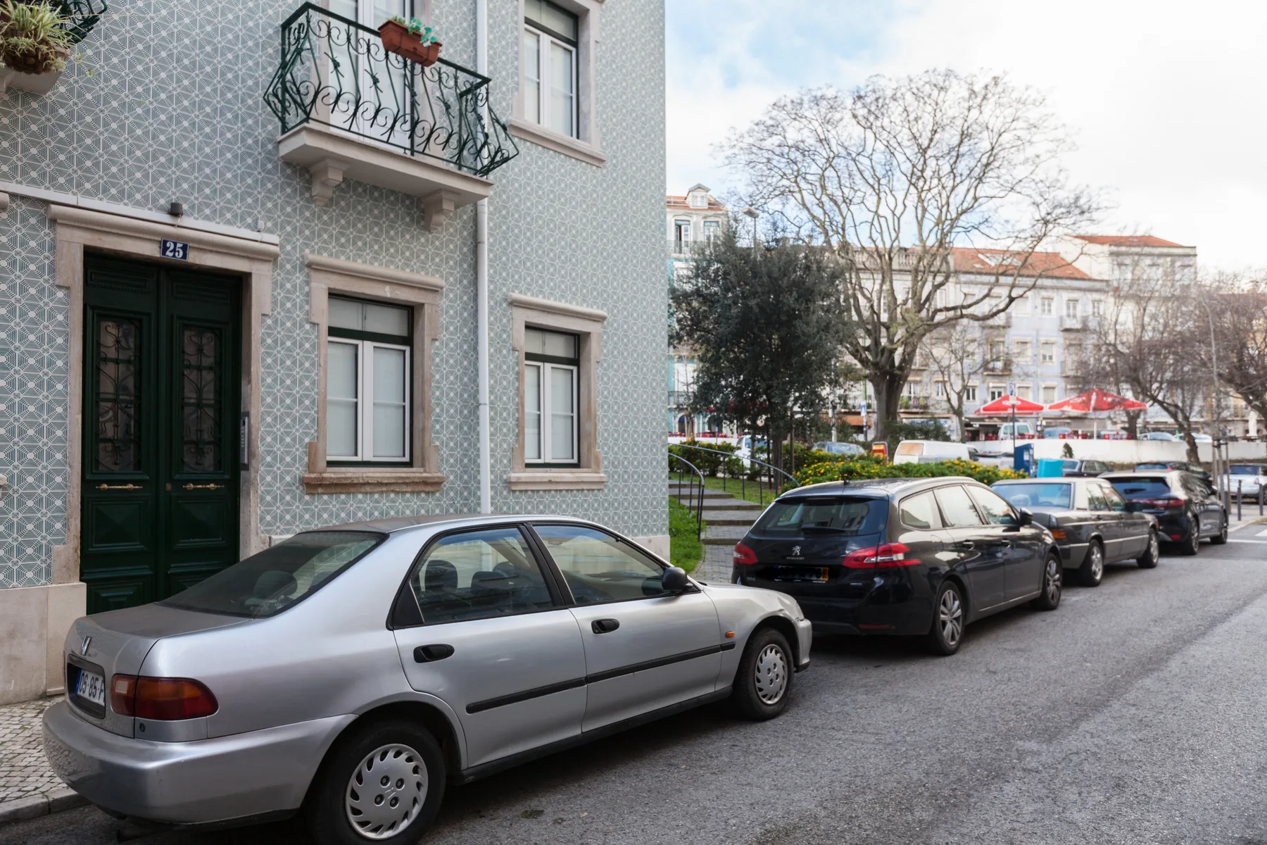 Street scene with parked cars beside a tiled building and a small balcony.