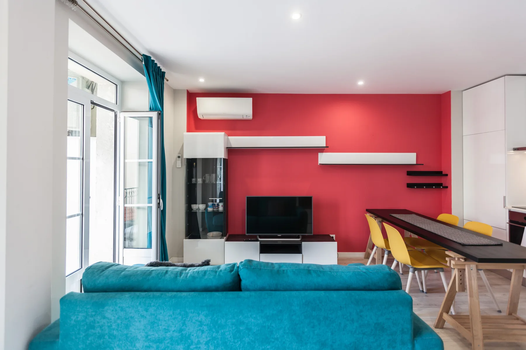 A colorful living and dining area with turquoise seating and a red accent wall.