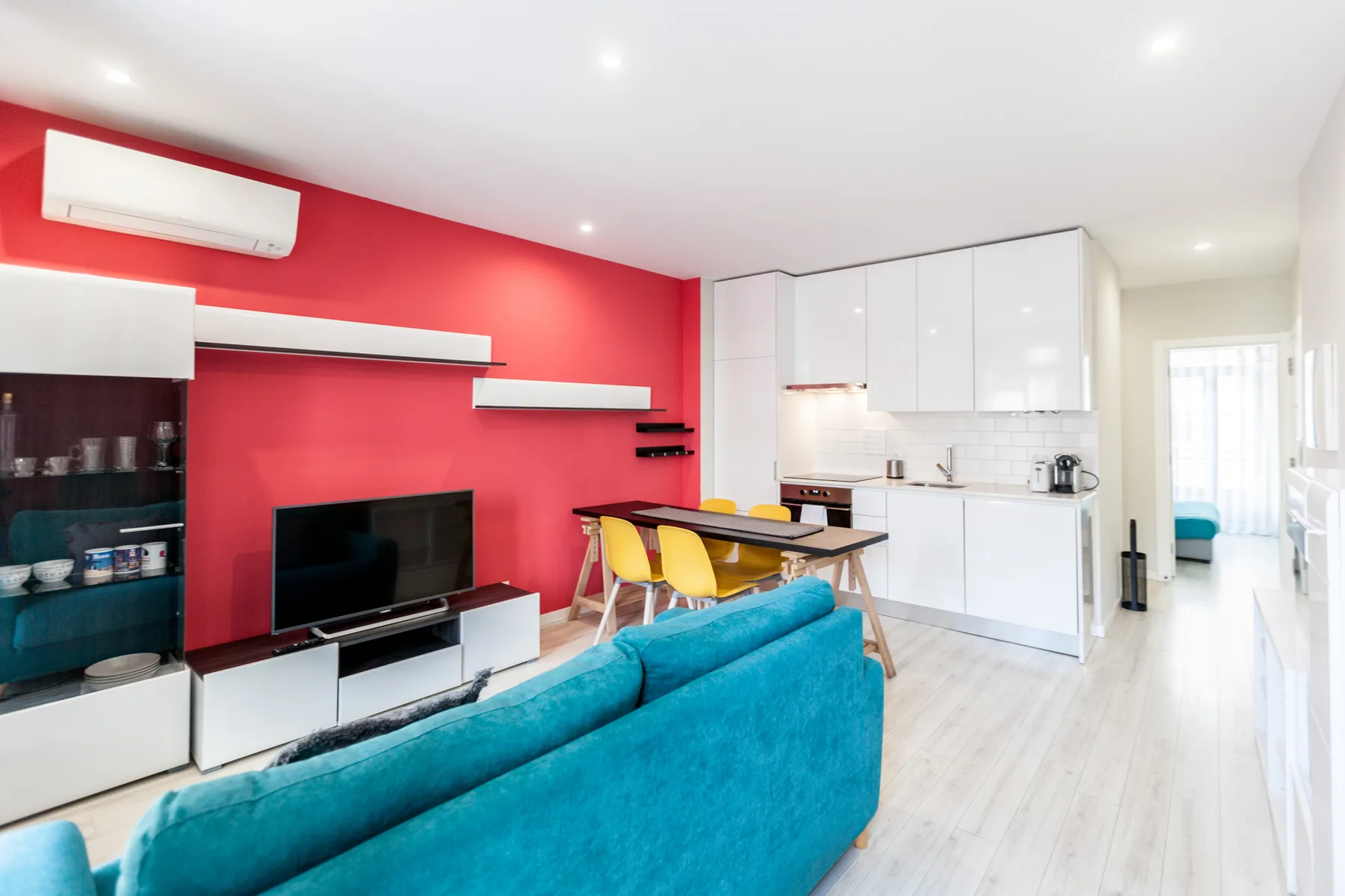 Living room and kitchen with a red accent wall and turquoise seating.