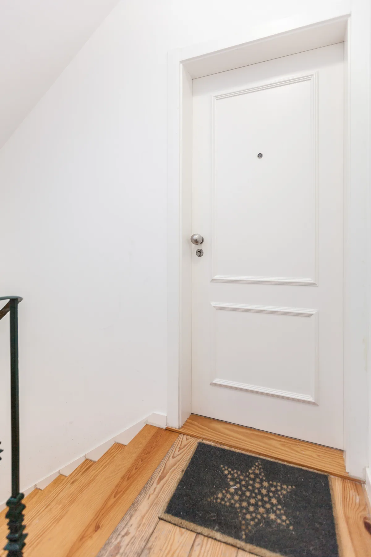 A white entry door opens onto a wooden staircase with a patterned doormat.