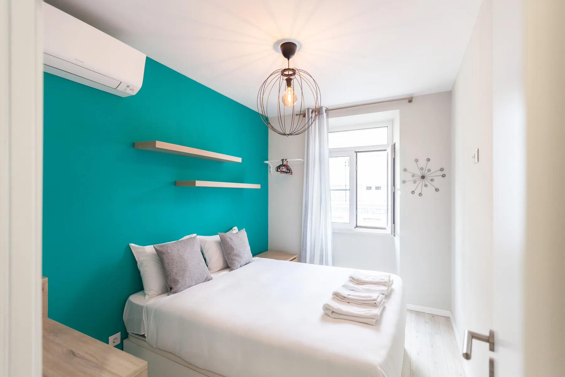 A bedroom with a bed against a bright teal accent wall.