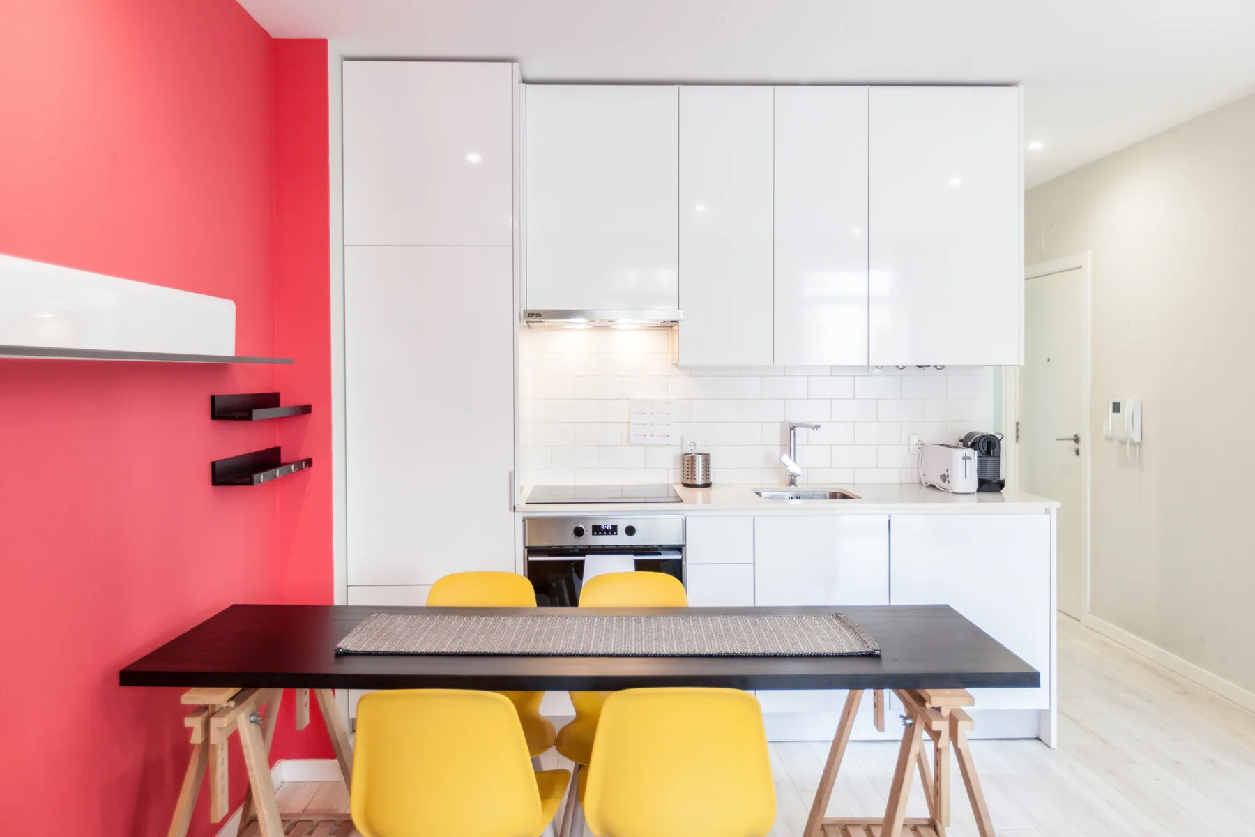 A compact kitchen and dining area with white cabinets, a dark table, and yellow seating.