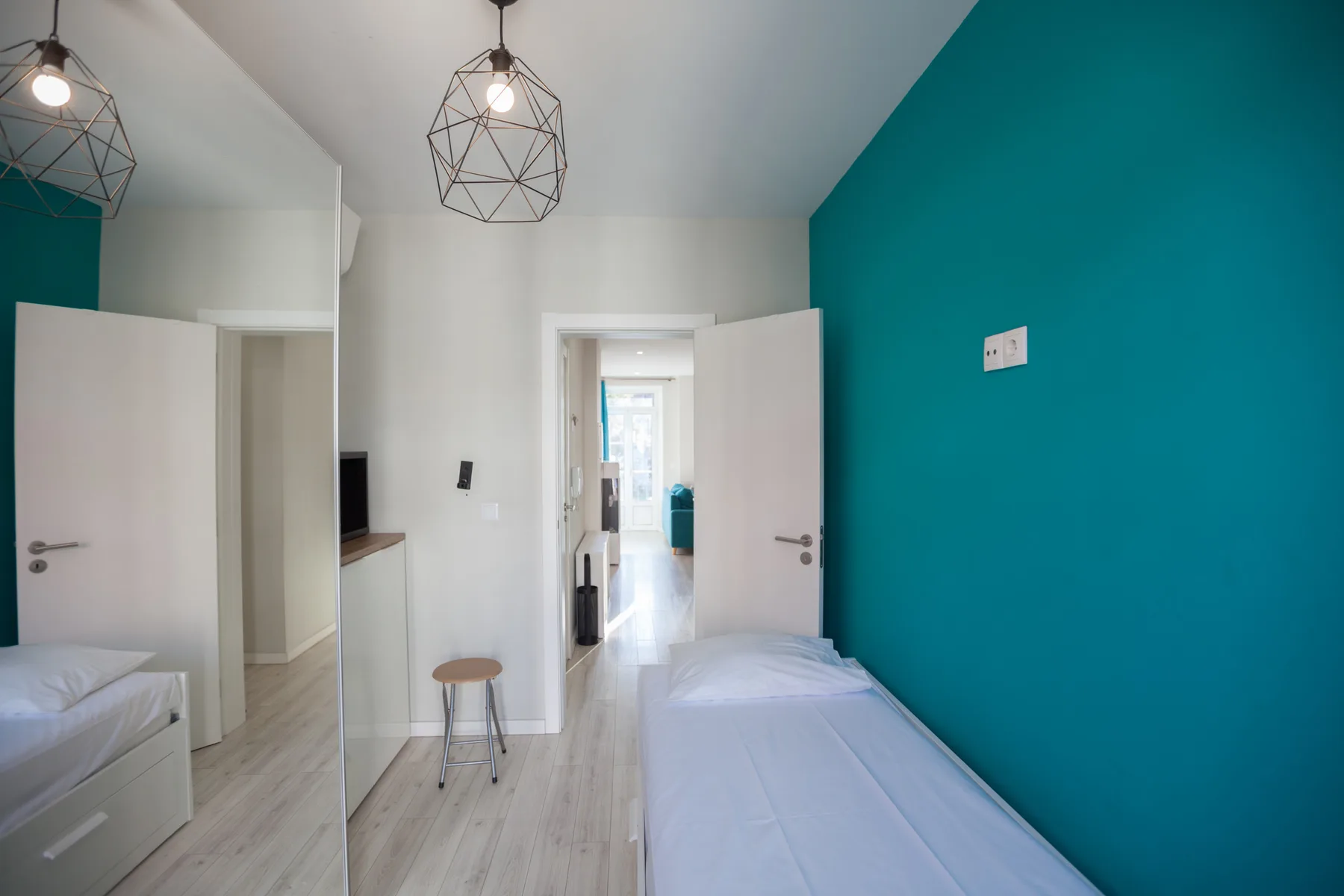 A bright bedroom with twin beds and a teal accent wall.