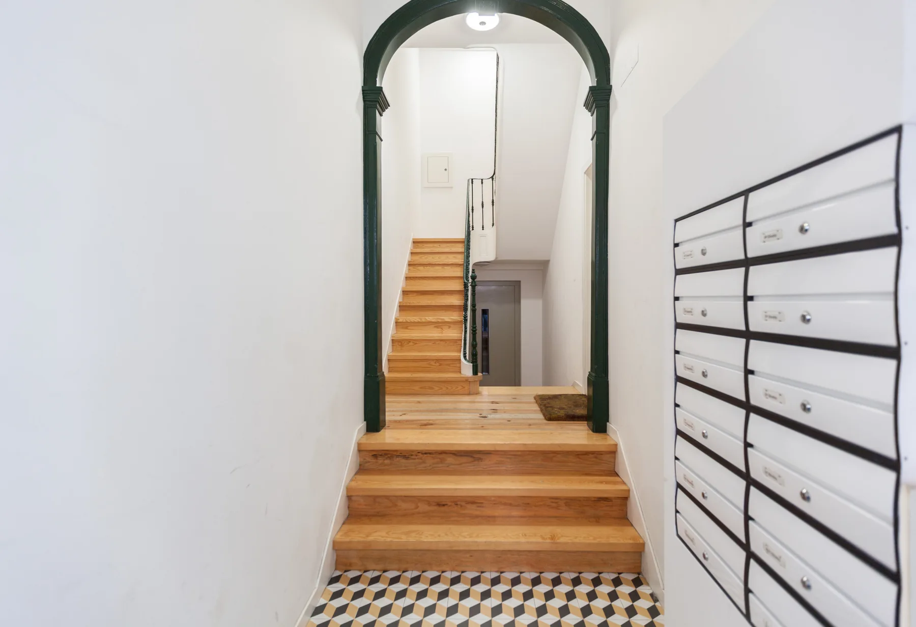 An interior hallway with wooden stairs, an arched doorway, and a wall of mailboxes.