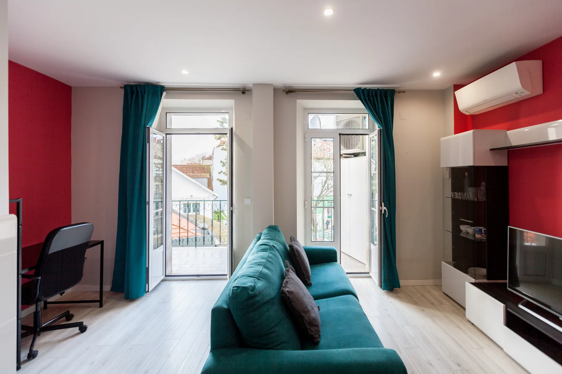 A colorful living room with teal seating and tall windows opening onto balconies.