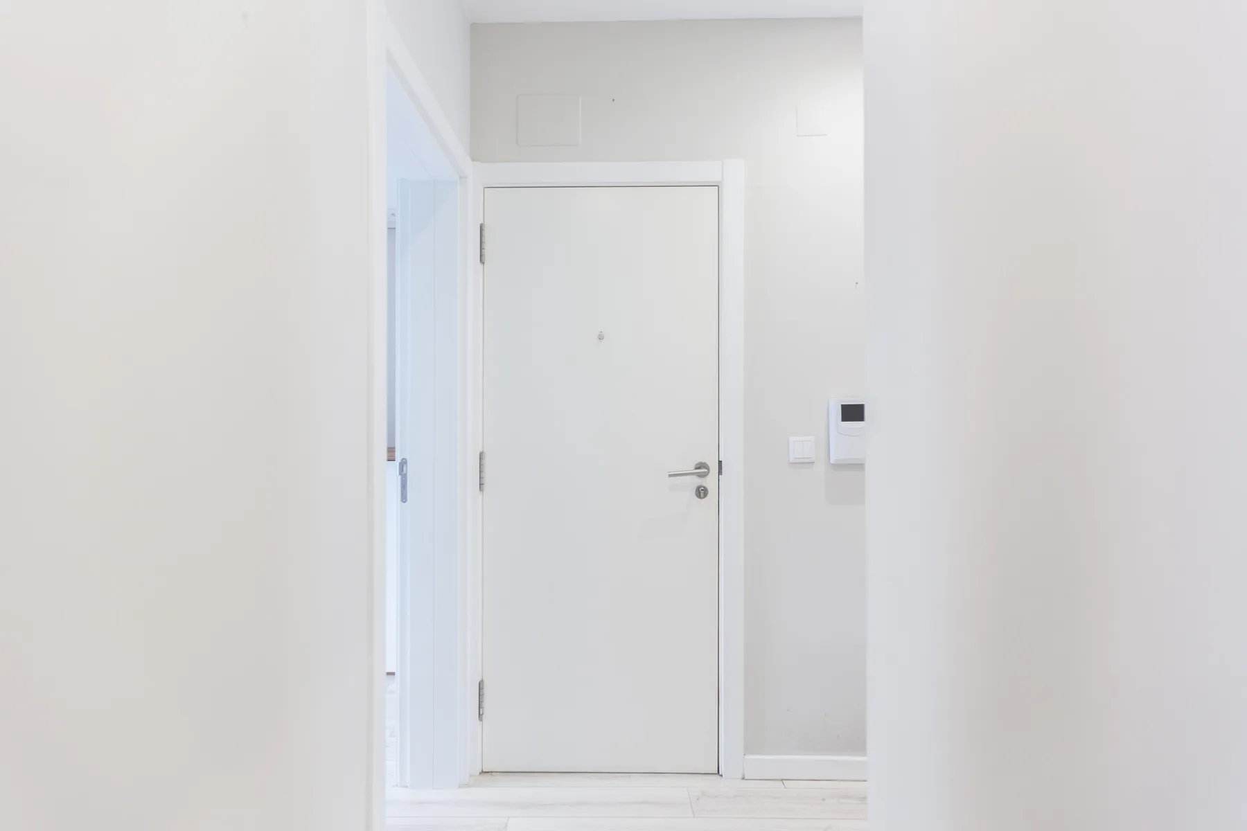 A bright white entryway with a closed door and wall controls.