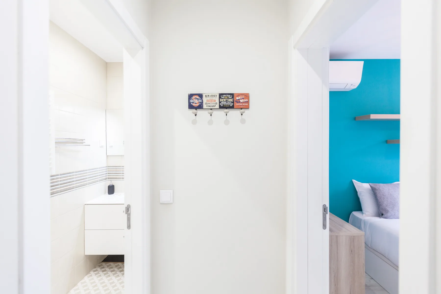 A bright hallway opens onto a bathroom and a bedroom with a turquoise wall.