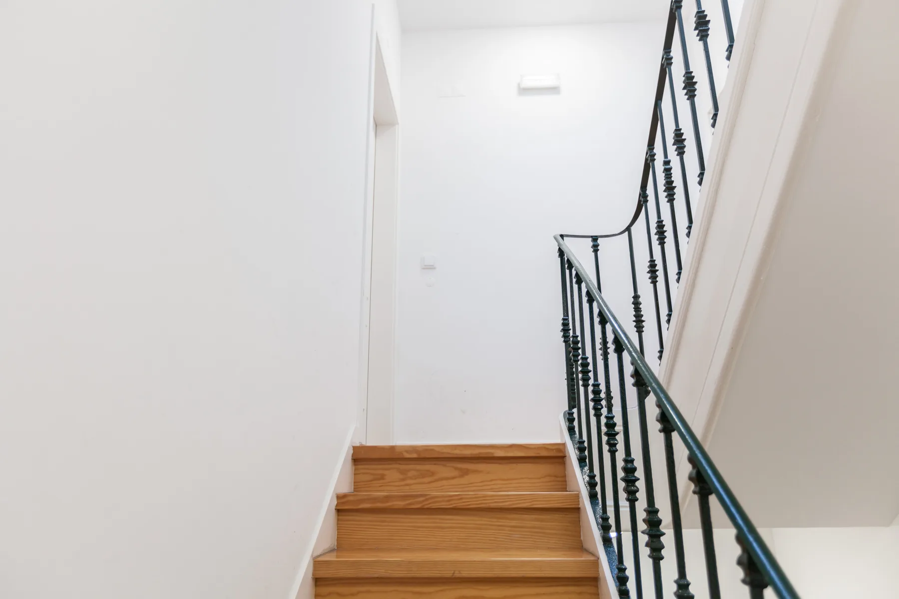 A bright interior staircase with wooden steps and a dark railing.