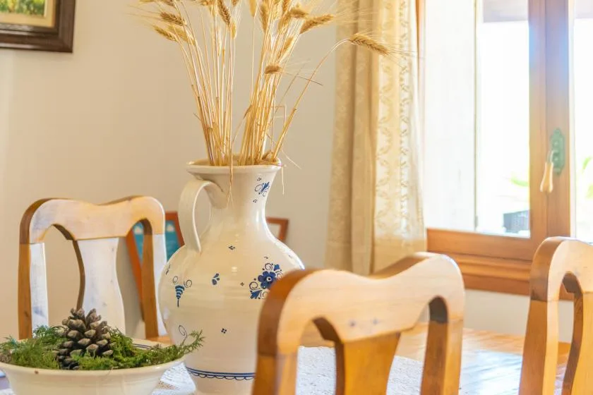 A dining area with wooden seating around a table and a vase of dried grasses.