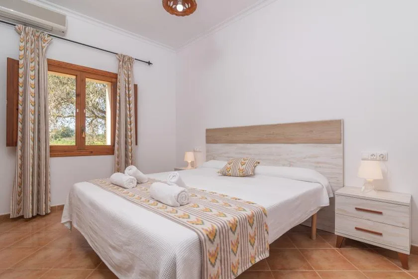 A bedroom with a neatly made bed and a window with patterned curtains.