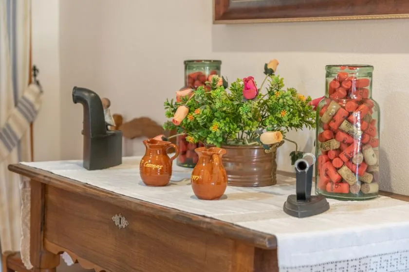 A wooden sideboard displays flower arrangements, small pottery, and glass jars.