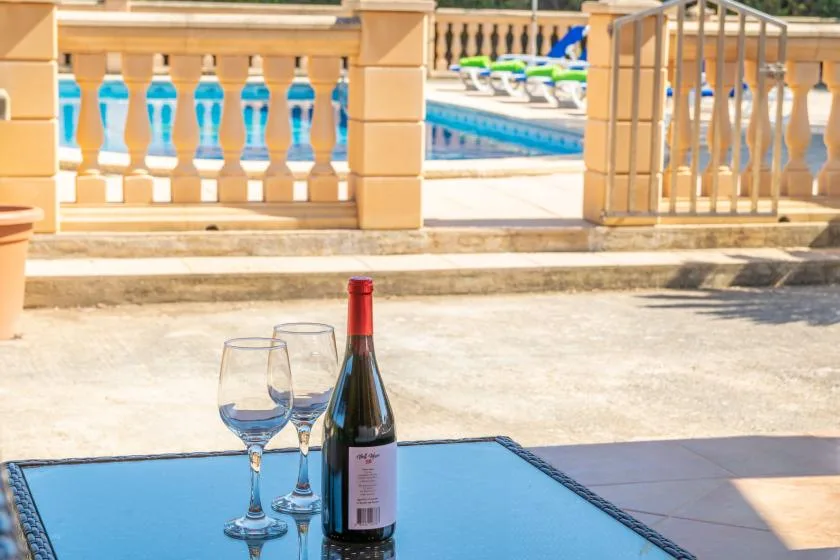 A bottle of wine and two glasses sit on a table beside a swimming pool.