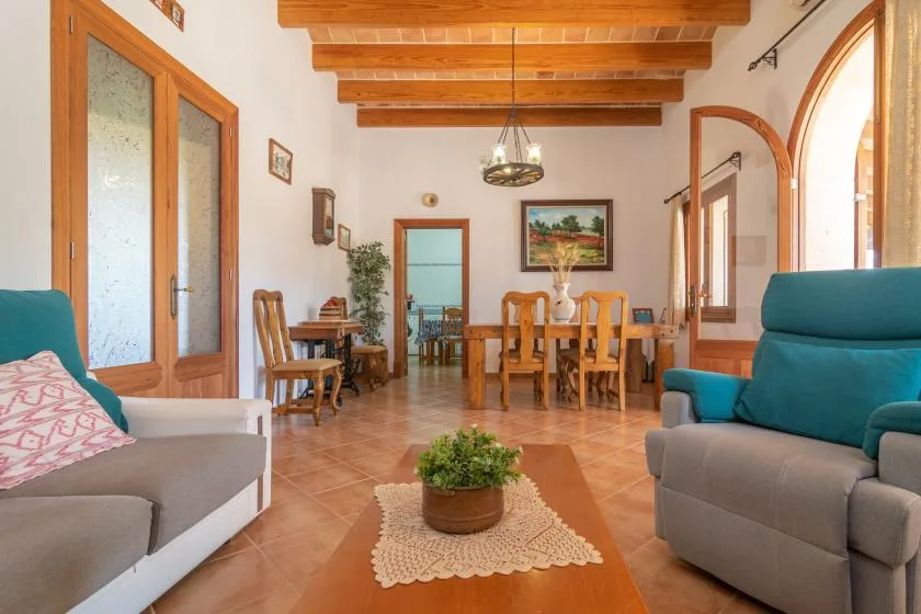 A bright living and dining area with seating, a wooden table, and exposed ceiling beams.