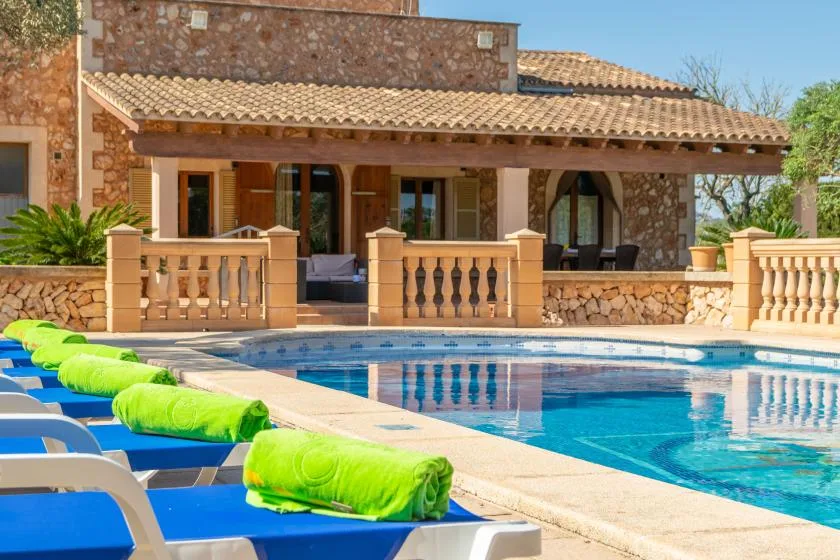 A swimming pool beside a stone house, with blue lounge chairs along the deck.