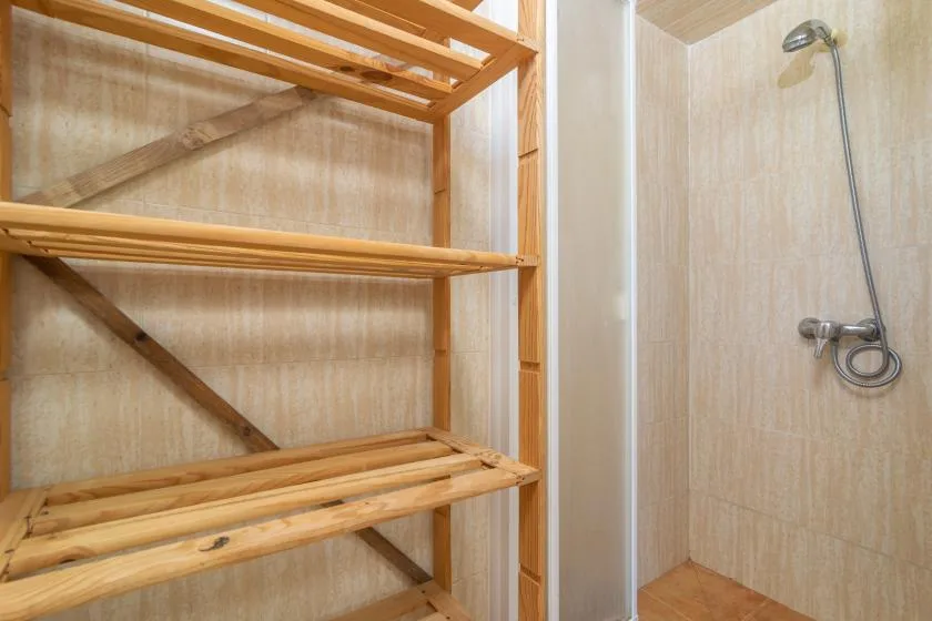A shower area beside a wooden shelving unit.