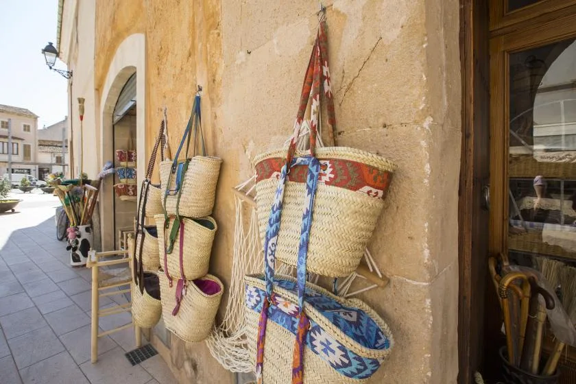 Woven baskets and colorful straps hang along a stone arcade beside a wooden doorway.