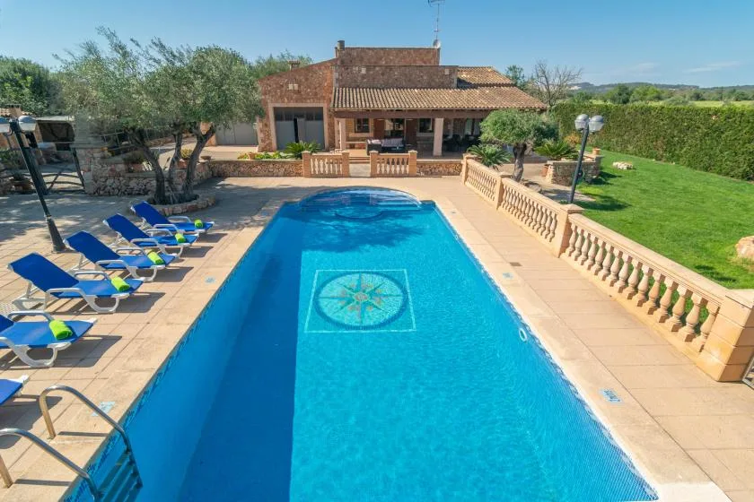 An outdoor swimming pool beside a tiled patio, lounge seating, and a covered terrace.