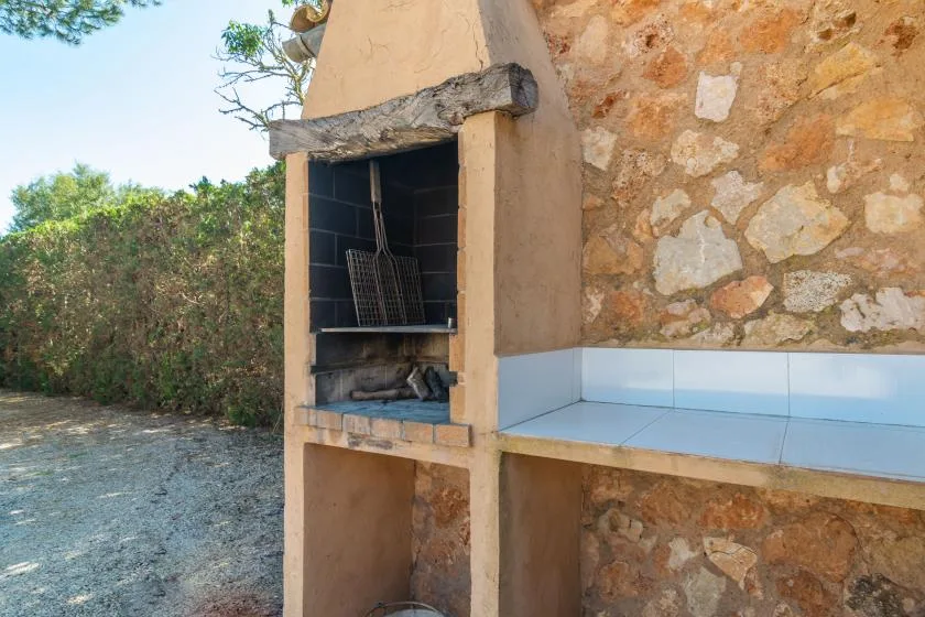 An outdoor masonry grill stands beside a tiled countertop and stone wall.