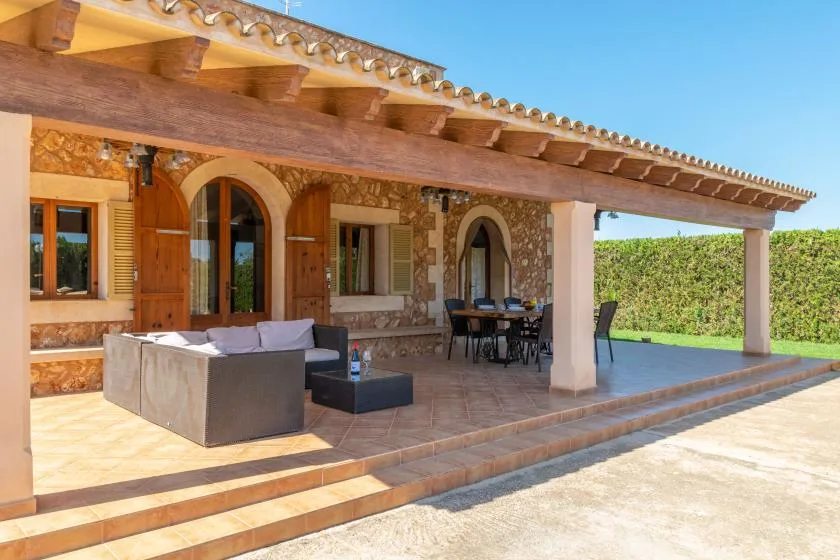 A covered outdoor patio with seating and a dining table beside the house.