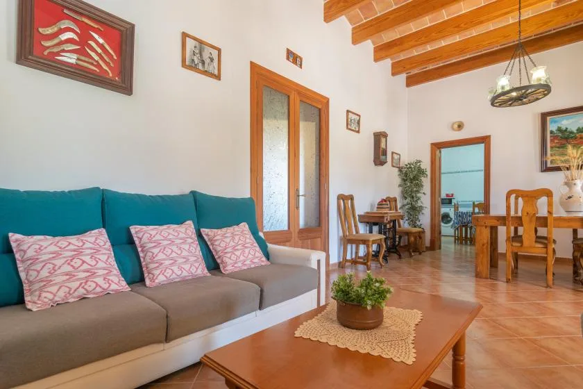 A living and dining area with teal seating, a wooden table, and exposed ceiling beams.