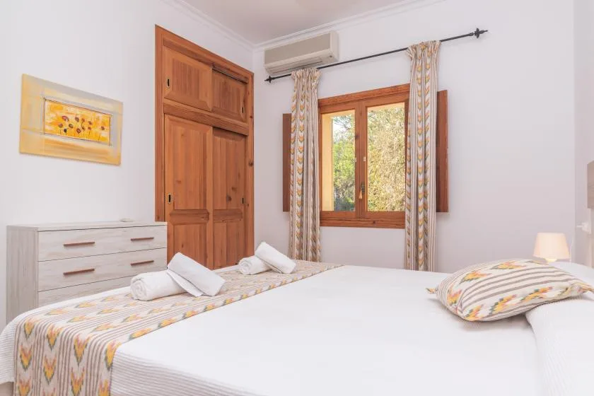 A bedroom with white bedding, wooden furniture, and a window with patterned curtains.