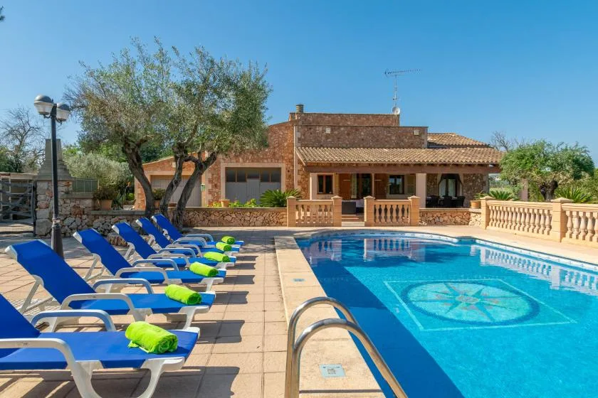 A swimming pool beside a patio with rows of blue lounge chairs and a house.