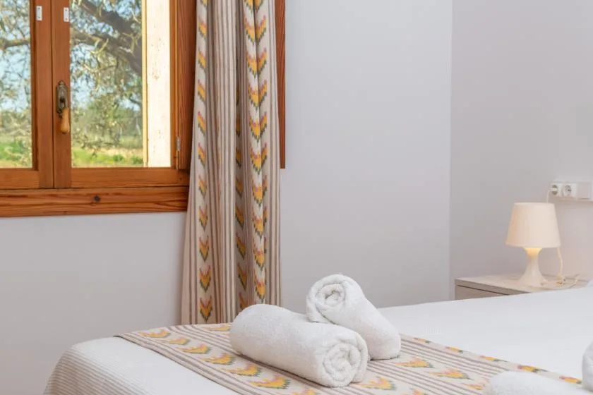 A bedroom with a neatly made bed and folded towels beside a window.