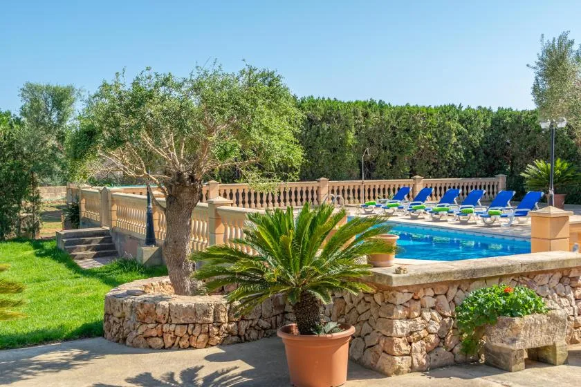An outdoor swimming pool bordered by stone walls, greenery, and rows of lounge chairs.
