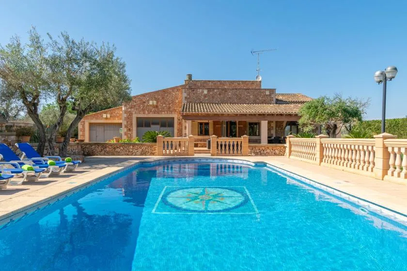 An outdoor swimming pool faces a stone house, with lounge seating beside the water.