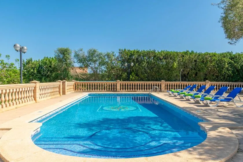 An outdoor swimming pool is surrounded by a paved deck and blue lounge chairs.