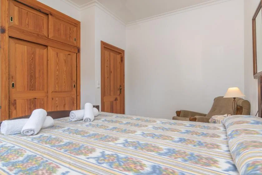 A bedroom with a patterned bedspread, wooden wardrobe, and bedside lamp.