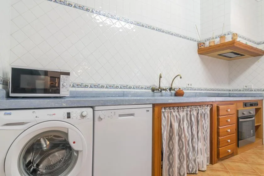 A tiled kitchen with a countertop, sink, washing machine, and built-in appliances.