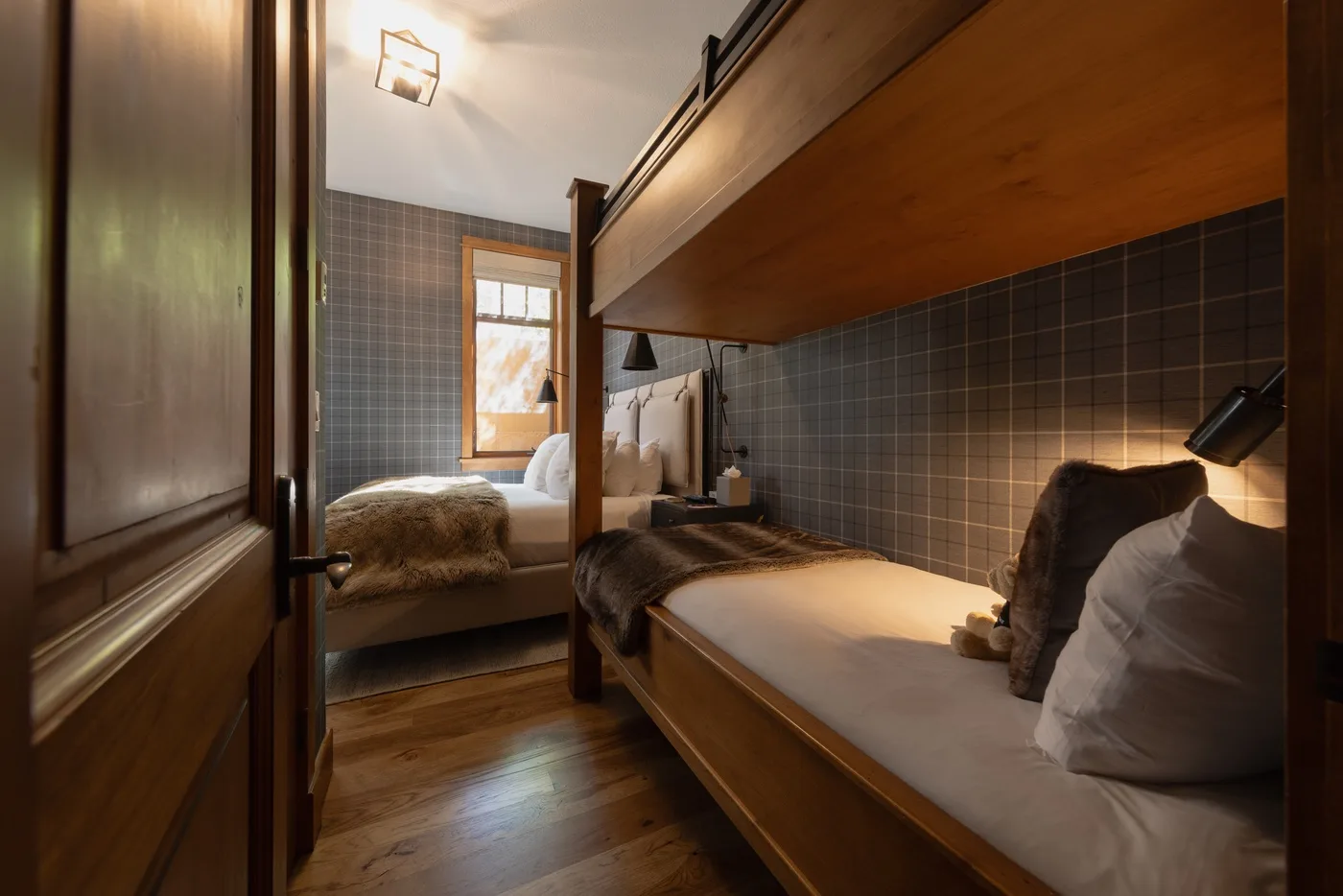 A bedroom with two beds, a window, and dark tiled walls.