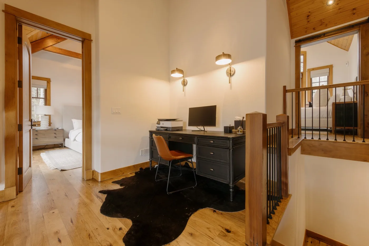 A bedroom workspace with a desk, chair, and computer beside a wood-floored sleeping area.