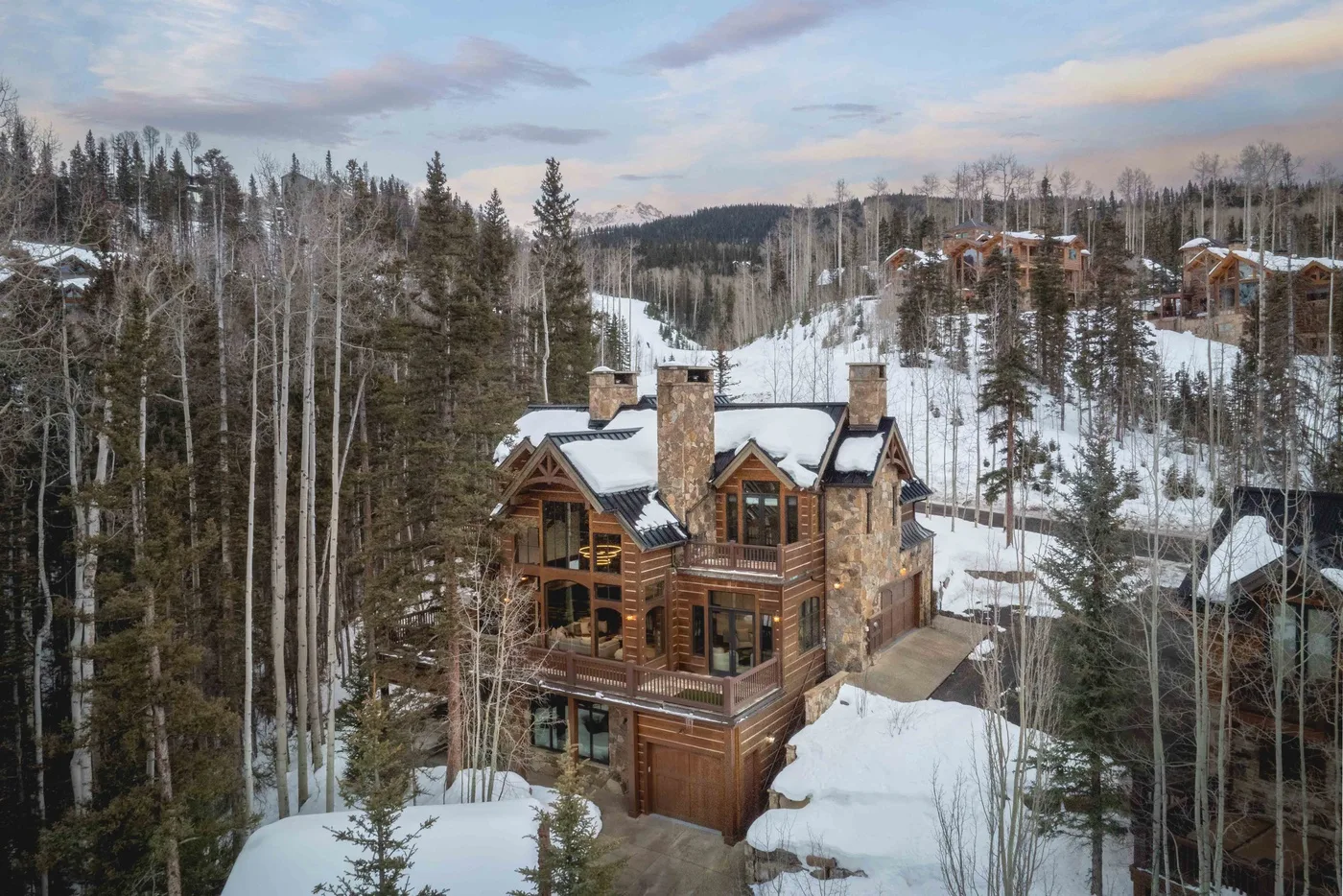 A large chalet stands among snow-covered trees on a wooded hillside.
