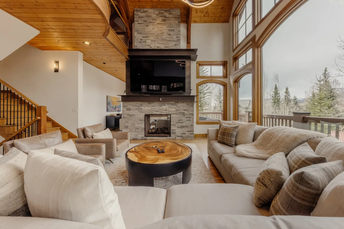 A spacious living room with seating arranged around a fireplace and large windows.