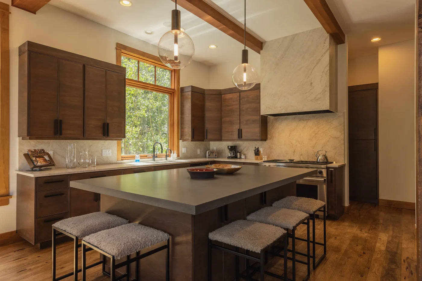 A bright kitchen with a large island and dark wood cabinets beneath exposed ceiling beams.