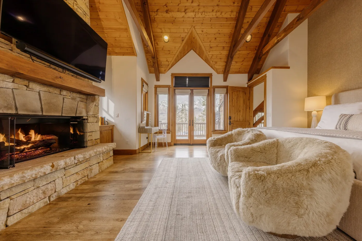A living room with a stone fireplace and plush seating beneath a wooden ceiling.