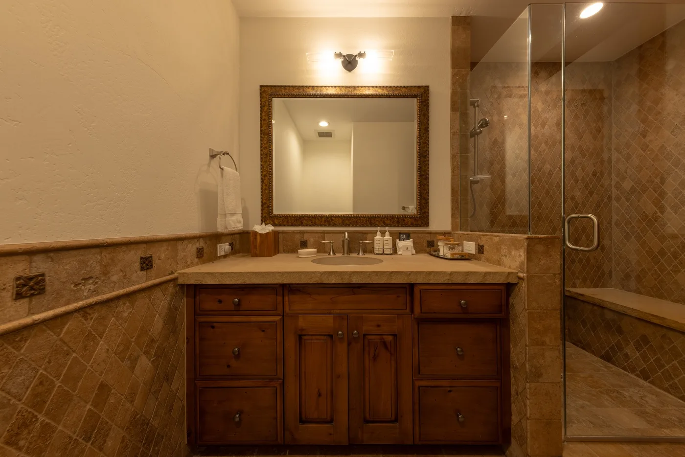 A bathroom vanity with a large mirror stands beside a glass-enclosed shower.
